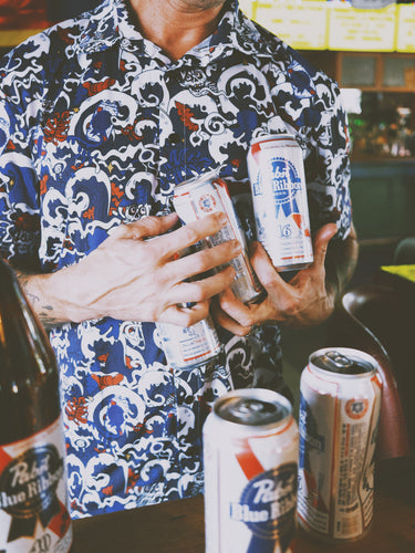 Person holding multiple beer cans in a bar setting