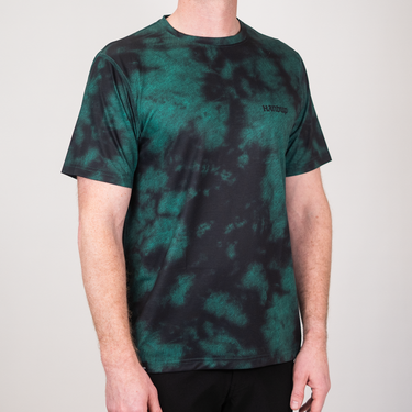 Person wearing a green and black tie-dye t-shirt with a brand logo on a plain background