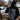 Person wearing a black and gray raincoat with a helmet and sunglasses, standing outdoors on a rainy day.
