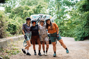 Four people posing with bicycles on a trail, with a van in the background.
